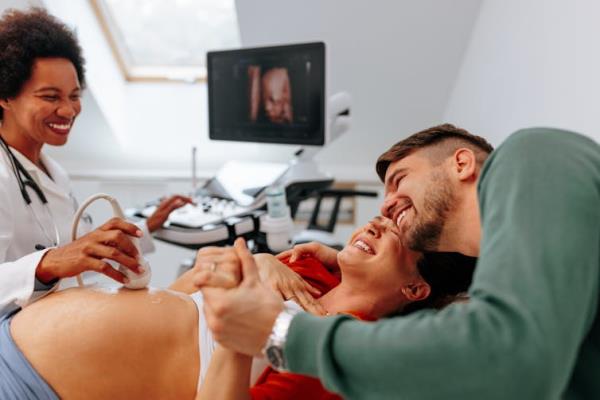 A happy pregnant woman is at the doctors office havin<em></em>g an ultrasound scan checkup done with her husband.