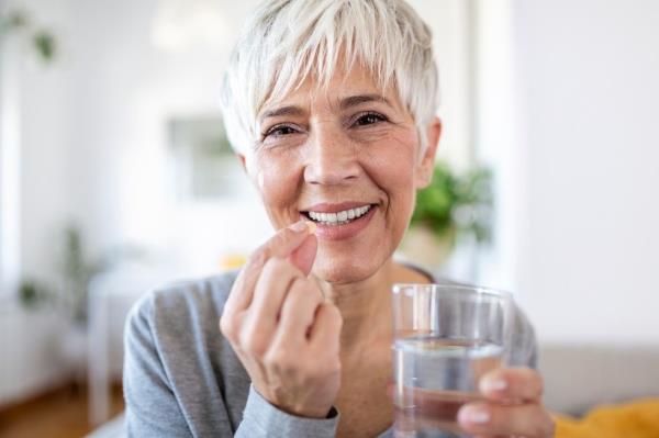 Senior woman holding omega-3 fish oil nutritio<em></em>nal supplement and glass of water in her hands.