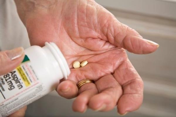 closeup of a senior person's hands taking two aspirin from the bottle