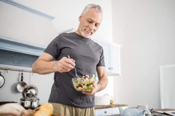 Older man eating a healthy salad in the kitchen