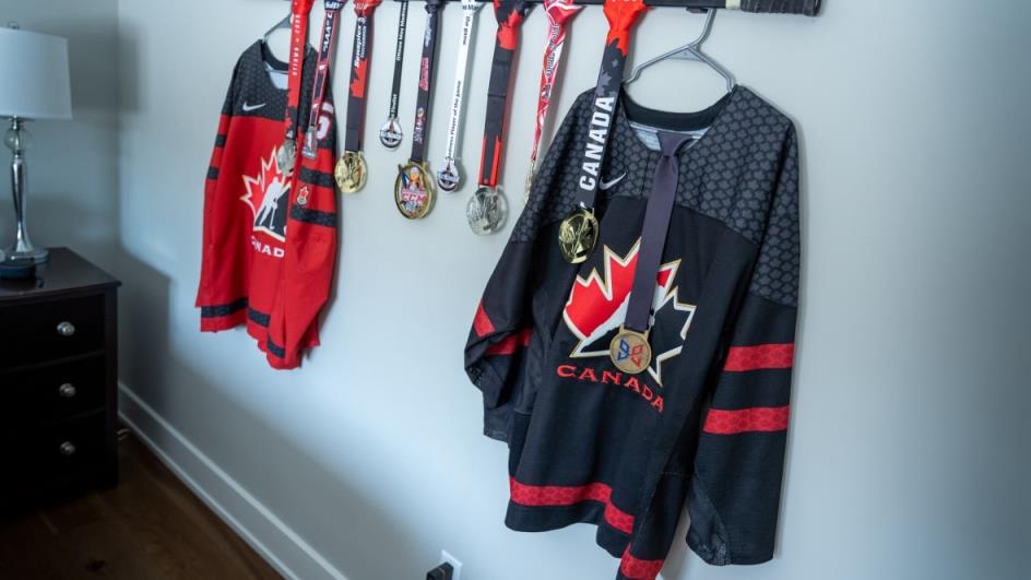 Jerseys and medals hanging from a hockey stick in someone's bedroom. 