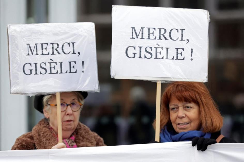 Two women hold  signs that say merci, gisele