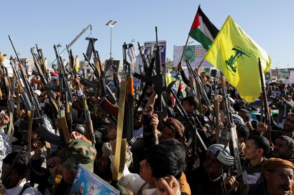 Dozens of men are shown holding up rifles and flags at an outdoor demonstration.
