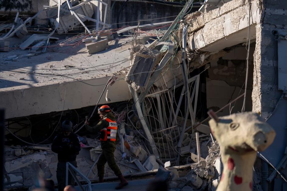 A helmeted worker in a reflective vest is shown standing near buckled co<em></em>ncrete and other debris.