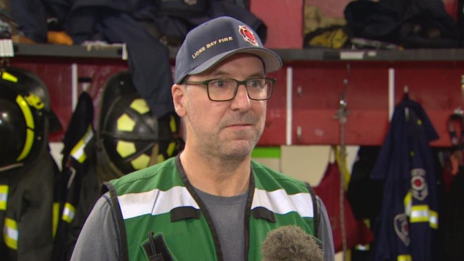 A man wearing a green high-vis vest speaks in a fire hall.