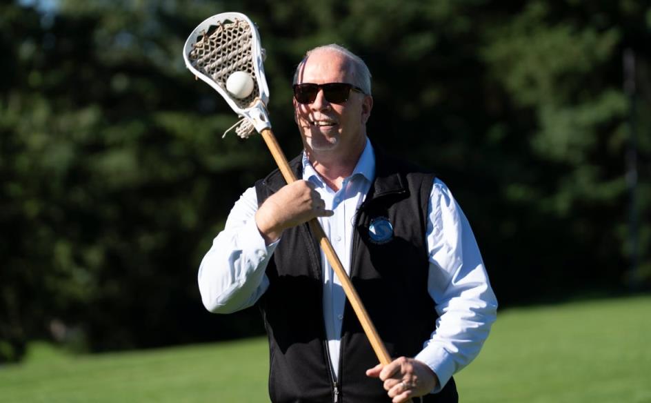A man catches a lacrosse ball with a stick on a sunny day.