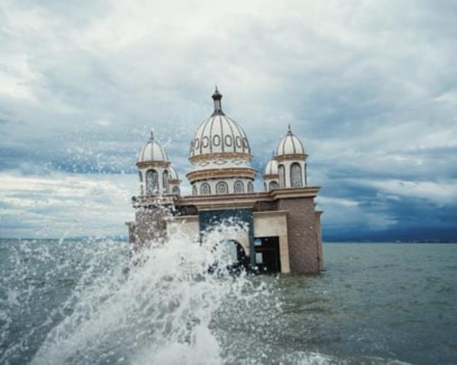 A wave crashes in front of a mosque half submerged in water
