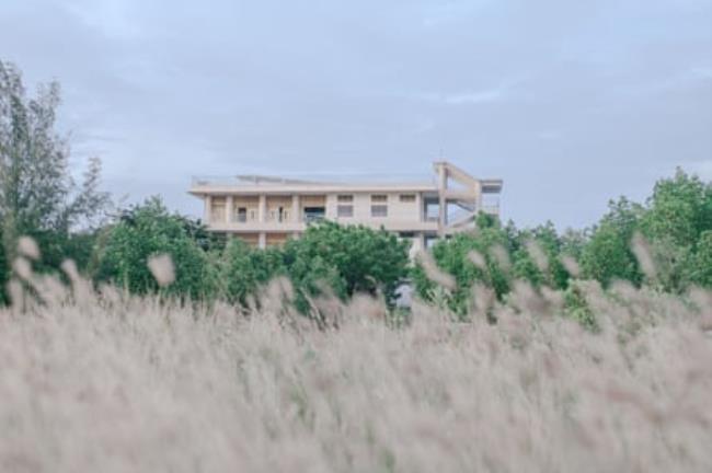 A low-rise building half hidden behind shrubs and grass in the foreground.