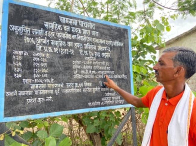 A middle-aged Indian man points to words written in an Indian s<em></em>cript on a blackboard