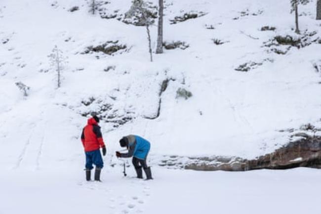 Two people check the depth of water in the ice in a snowy landscape