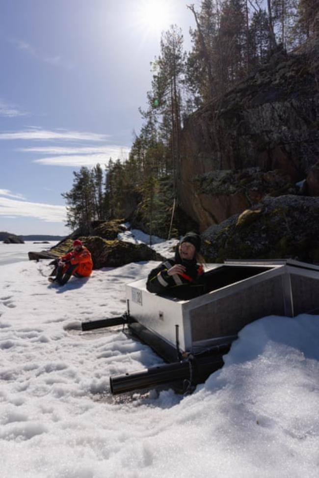 A woman stands in a seal den made from a wooden box 