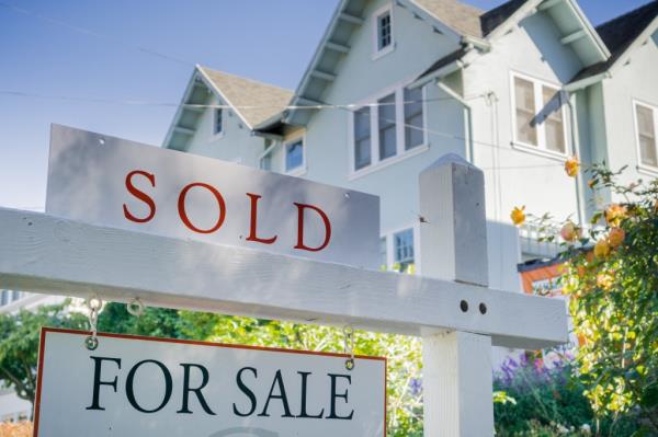 Sold sign on a white post in front of a house in a residential neighborhood in California
