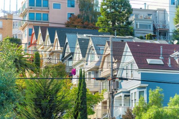 Row of colorful blue, beige, red, yellow, and white houses in a modern San Francisco neighborhood with visible power lines during midday.