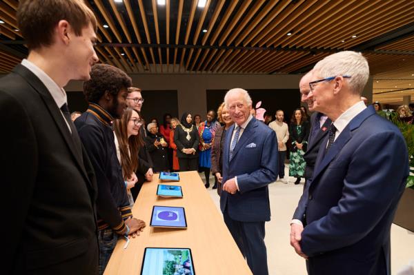 King Charles and Tim Cook meet alumni from The King's Trust, who stand behind a table with iPad devices.