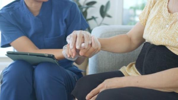 An aged care worker holding a woman’s hand during a home visit