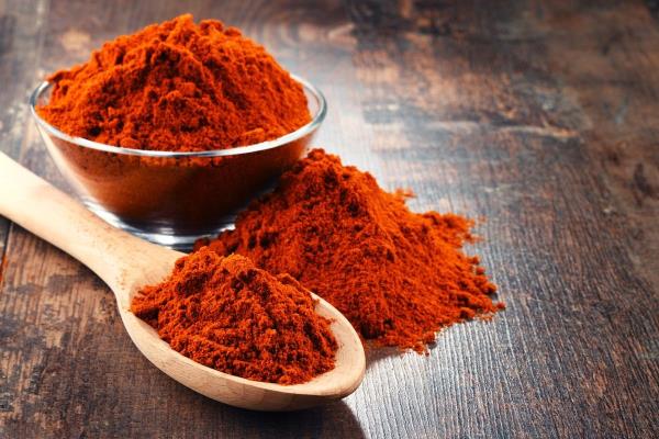 Spoon and bowl of cayenne pepper powder on wooden table