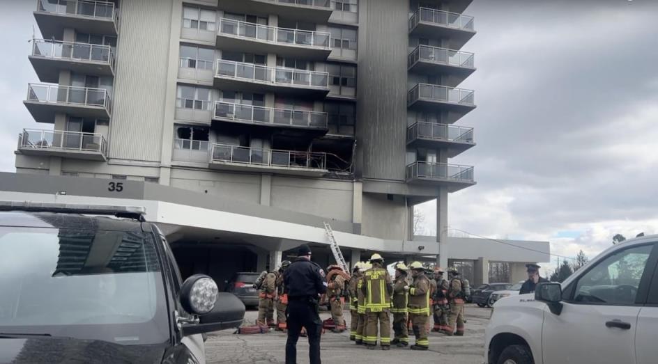Fire fighters stand in front of a blackened building. 