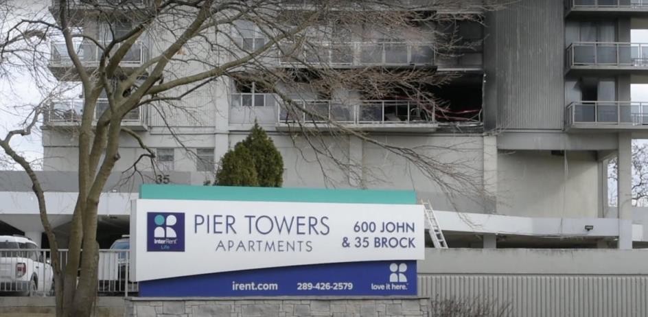 An apartment building sign in front of a building with at least one unit completely destroyed by fire. 