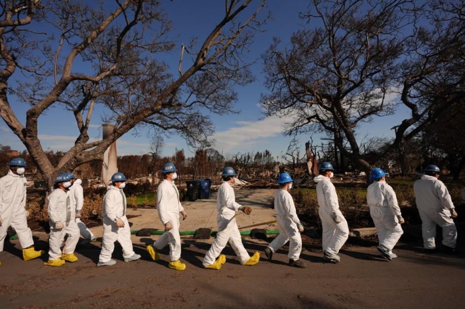 a<em></em>bout 10 people in protective suits, masks and wearing helmets walk in array outside.