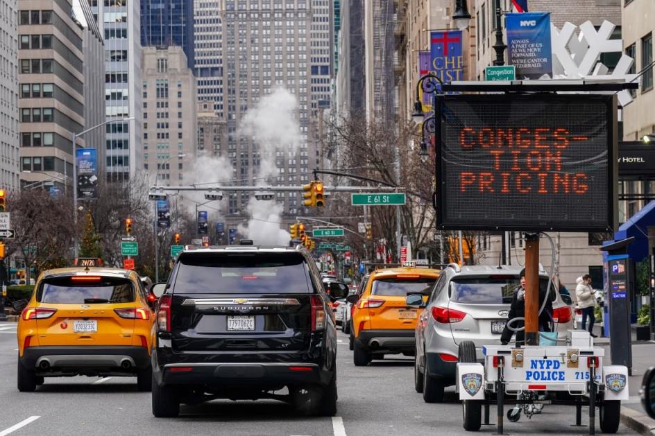 A sign that reads co<em></em>ngestion pricing sits on the side of a busy Manhattan road.