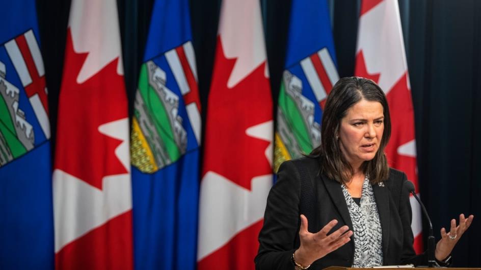 Premier Danielle Smith stands at the right end of a row of Albertan and Canadian flags.