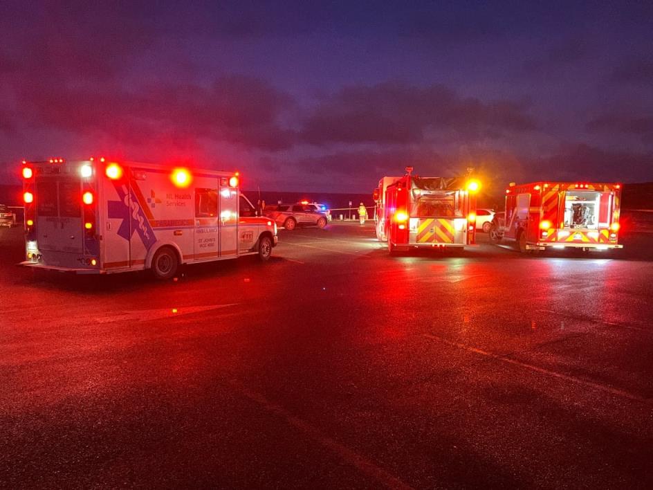 Several emergency vehicles including fire trucks and an ambulance sit on a parking lot.