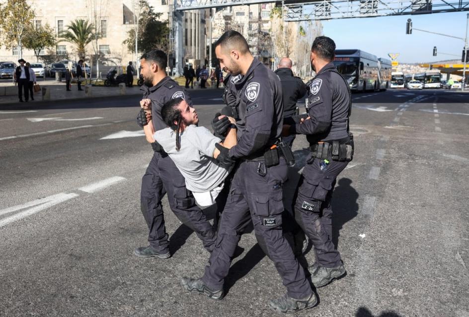 A man in a grey t-shirt is carried on a street by police officers