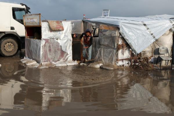 A displaced Palestinian man removes water at a tent camp